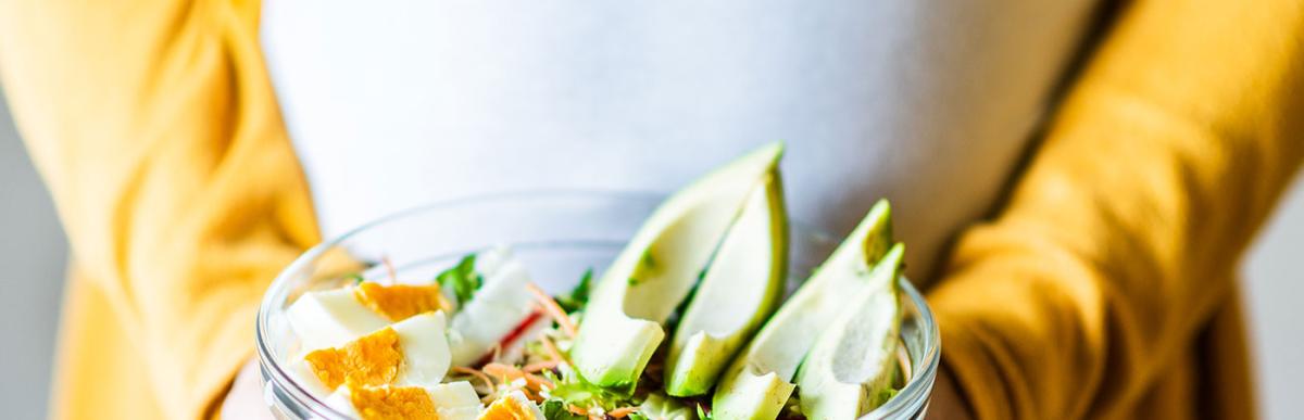 Pregnancy and healthy nutrition. Close-up of a pregnant woman's belly, holding vegetable salad.