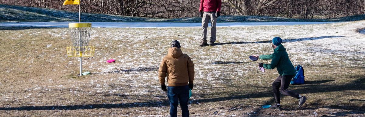 three people playing winter disc golf on a snowy golf course