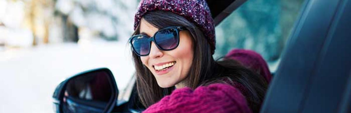 Women smiling while driving car in winter wearing knitted hat and sunglasses
