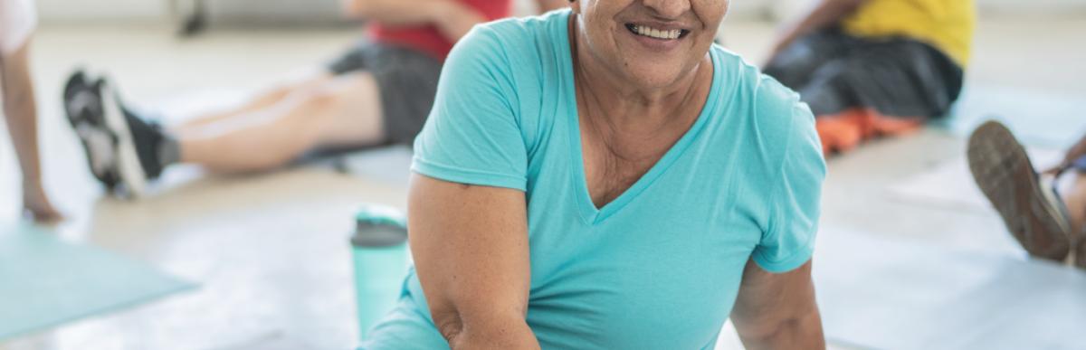 An older adult woman stretches on a mat while smiling