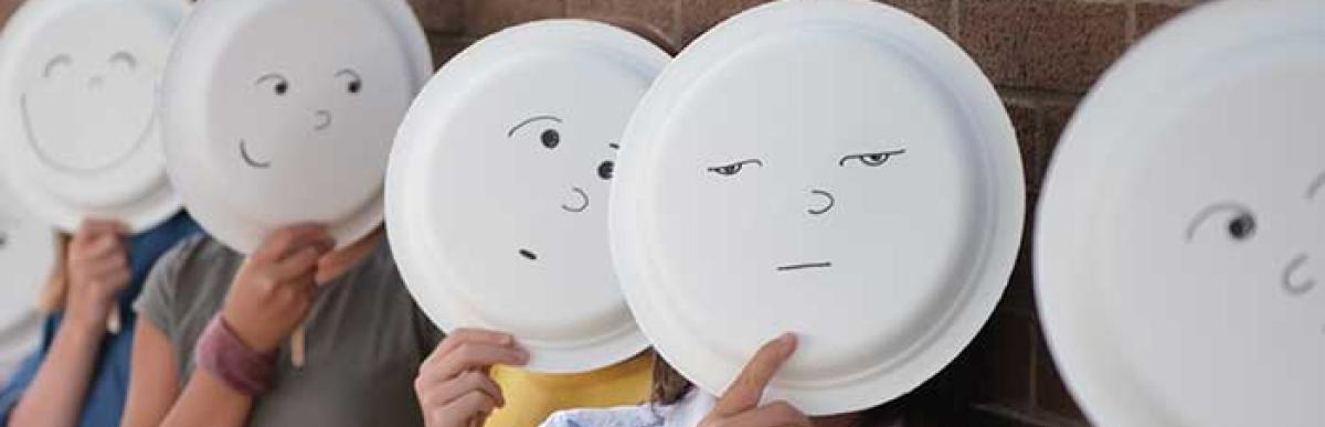 Children holding paper plates over their faces with drawn faces showing different emotions