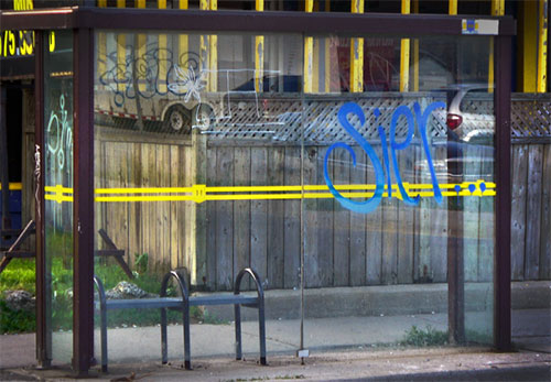 Image of a bus shelter with spray paint graffiti on the glass wall