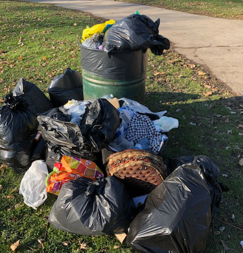 Photo of an overflowing trashcan, surrounded by bags of trash.