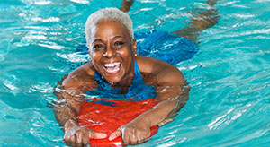 Older woman in a swimming pool holding a floatation/flutter board
