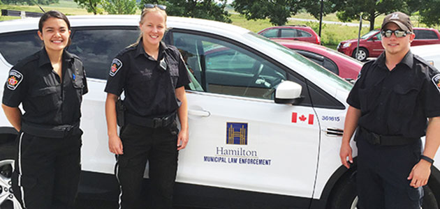 2 Municipal Law Officers in uniform standing beside city vehicle