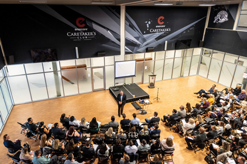 Room with people sitting in chairs watching a person give a presentation