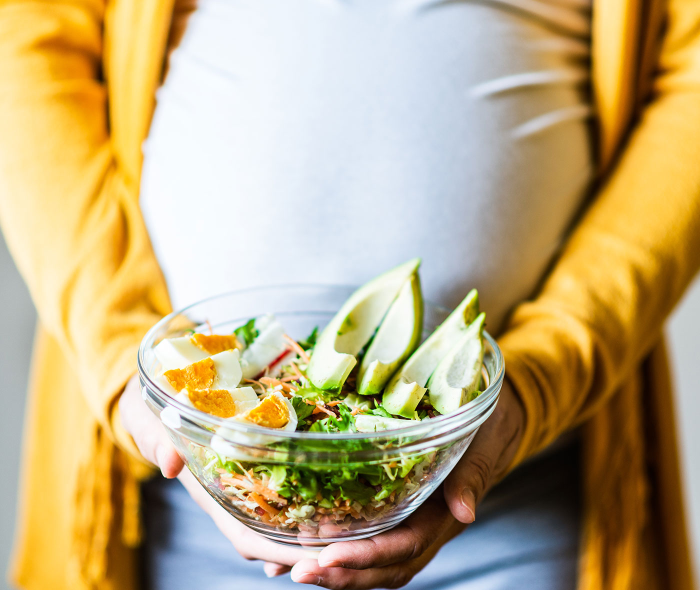 Pregnancy and healthy nutrition. Close-up of a pregnant woman's belly, holding vegetable salad.