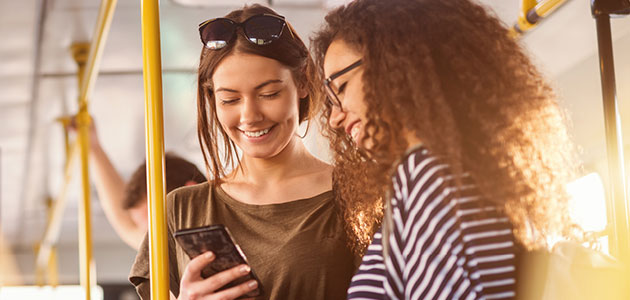 Two women riding the bus looking at cell phone and smiling