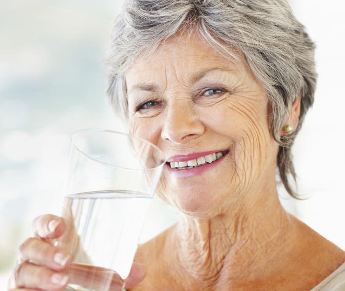 Older woman smiling drinking a glass of water