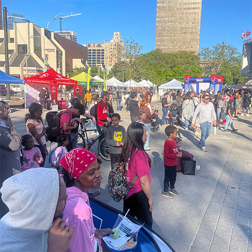 A crowd of smiling people of all ages gather outside of Hamilton City Hall for Newcomer Day