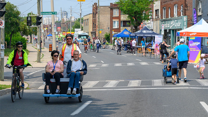 Two peopler riding on a pedi-bike, and a person on a bike on King Street during Open Streets