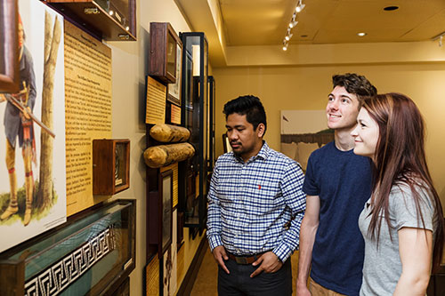 Three people looking at a display on the wall inside of the Hamilton Military Museum