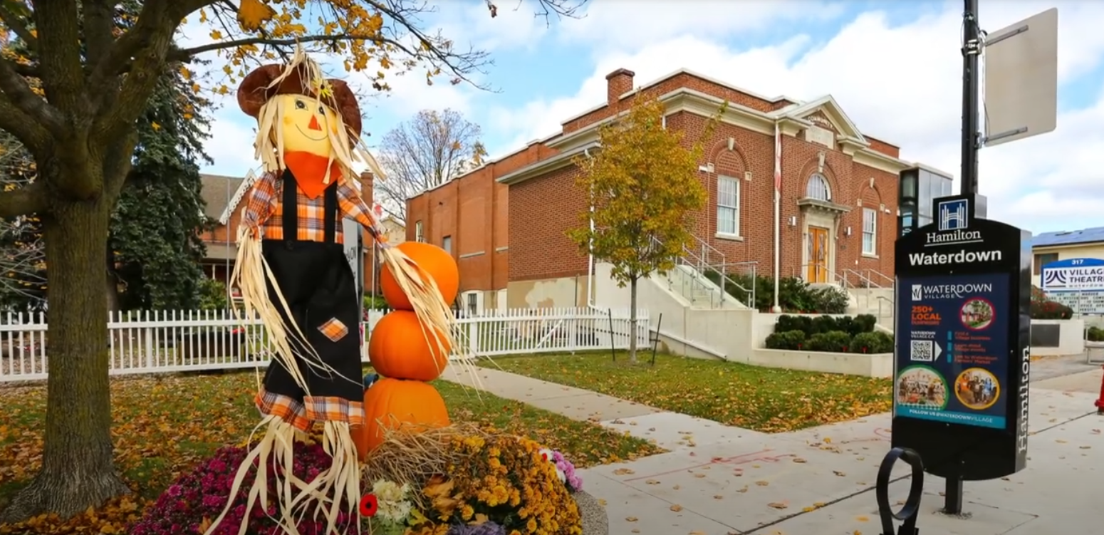 Scarecrow decoration on a street post and stack of pumpkins