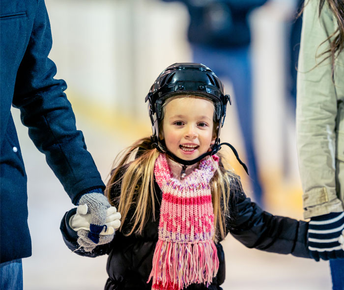 Little girl ice skating and holding her parents hands
