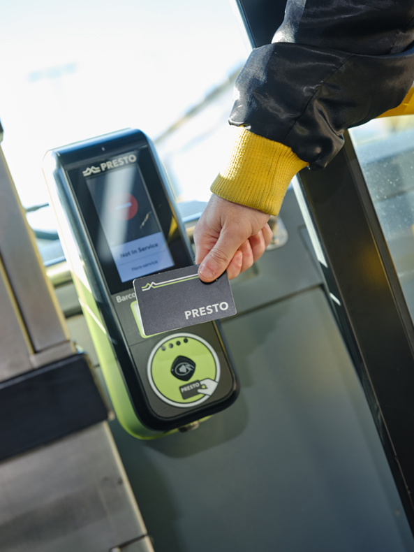 Person's hand holding a PRESTO card up to a card reader on an HSR bus