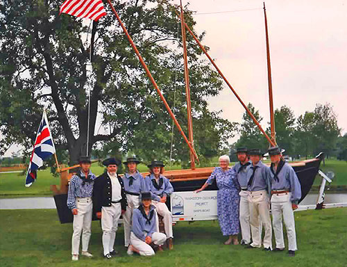 people in period costume standing next to a boat
