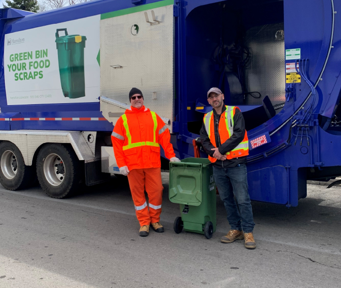 two waste employees standing in front of garbage truck