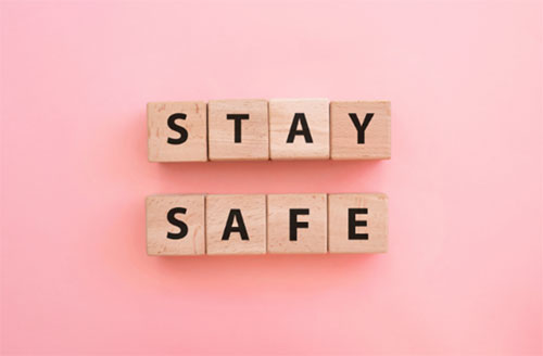 Wooden scrabble tiles spelling out "Stay Safe" on a pink background
