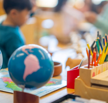 Close up of a classroom with a globe, pencil crayons in the foreground and an out of focus child in the background
