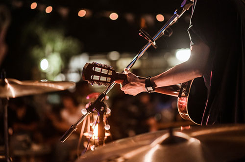 musician playing guitar and singing into microphone on a lit stage