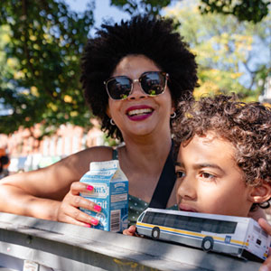 A woman and a child holding a toy HSR bus smile at the camera