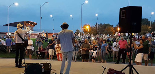 a band plays on the waterfront stage as people look on