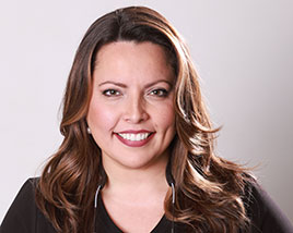 Headshot of Cynthia Meneses, A woman from the shoulders up, with long brown slightly wavy hair, smiling at the camera.