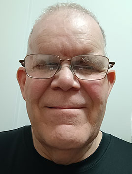 Headshot of Derm Tilley: A man from the shoulders up, with short grey hair, smiling at the camera.