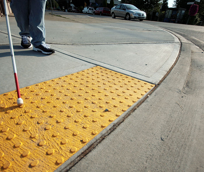 Person walking with guide cane on sidewalk with tactile surface domes