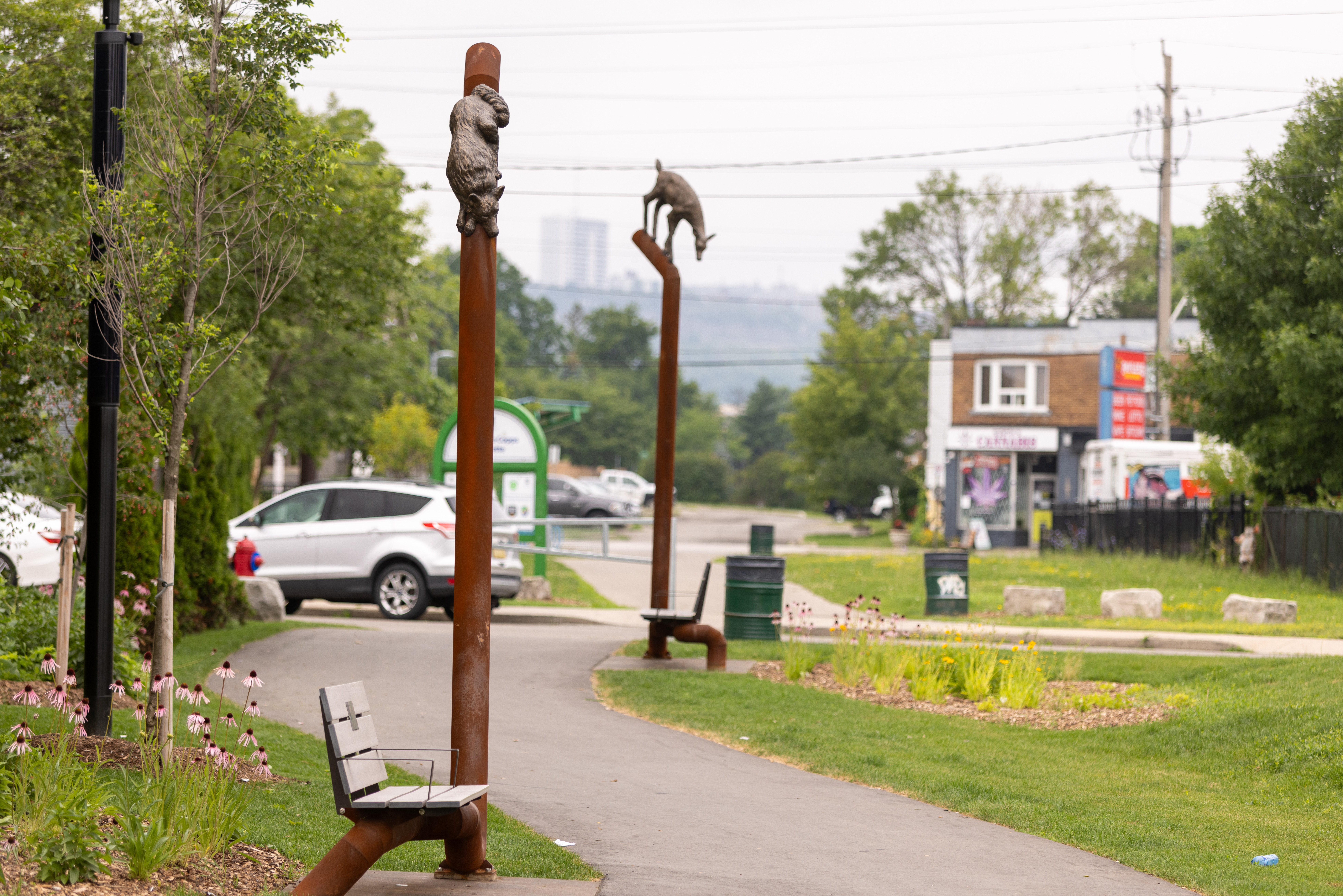Two park benches with poles integrated into them. Atop the poles re sculptures of animals. "A Shared Trail" by Brandon Vickerd