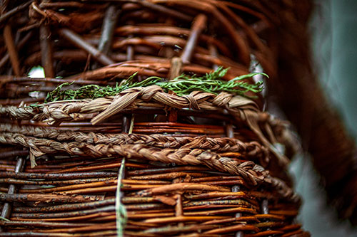A detail close-up look of "Right to Repossess" sculpture, made out of willow, a cedar post, corn husk, wood, clay, material, and ribbon.