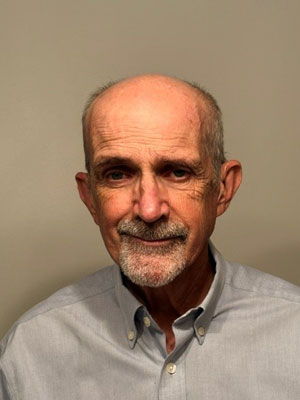 Man with grey hair and goatee and a small smile wearing a light grey collared, button-up shirt