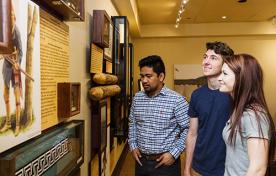 Three people looking at a display on the wall inside of the Hamilton Military Museum