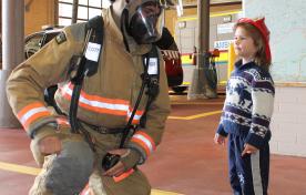 child with a firefighter in full uniform and gear