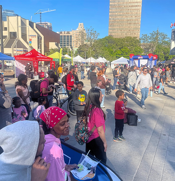 A crowd of smiling people of all ages gather outside of Hamilton City Hall for Newcomer Day