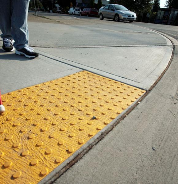 Person walking with guide cane on sidewalk with tactile surface domes