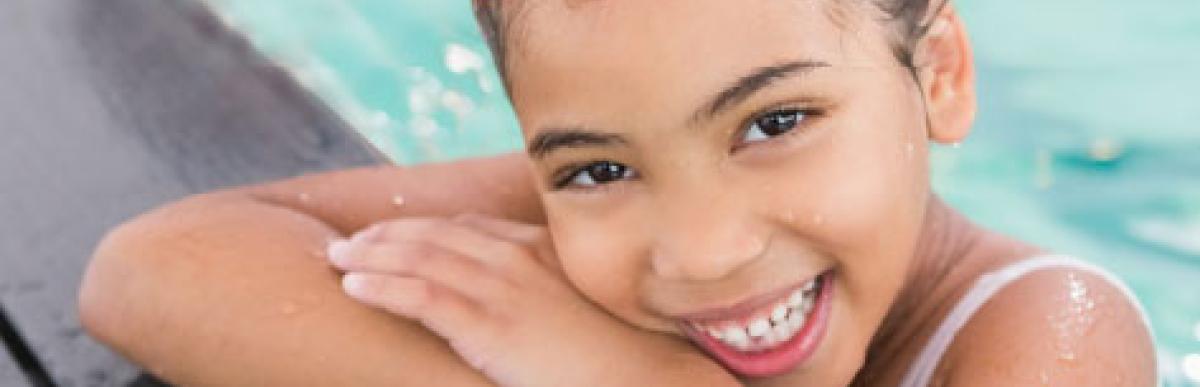 Smiling young girl at the edge of the pool wearing swim goggles and a swim cap