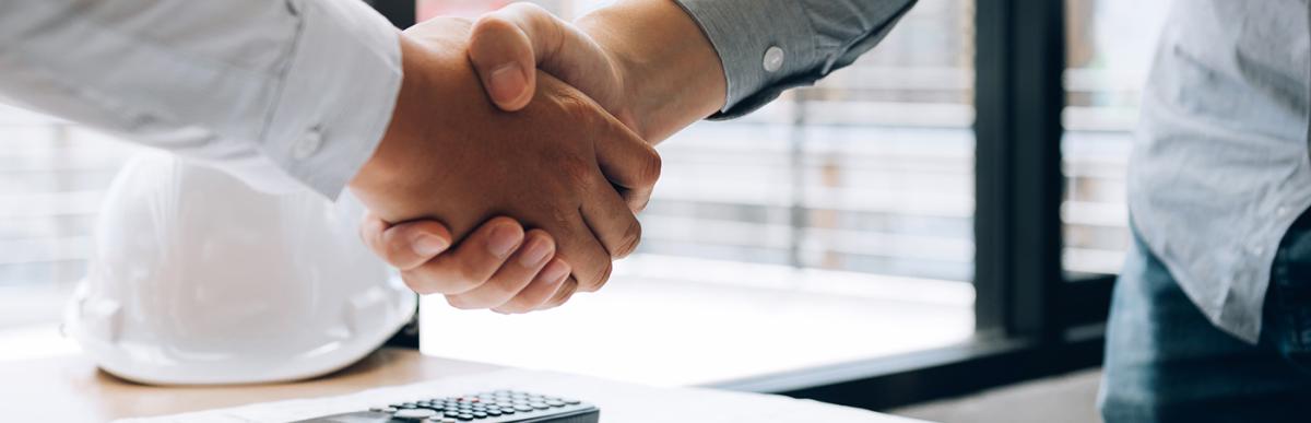 Two people shaking hands over drawings and plans for construction