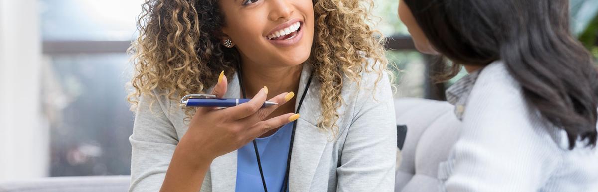 Positive young female gestures as she talks with a female client. The woman smiles warmly as she talks with the young woman.