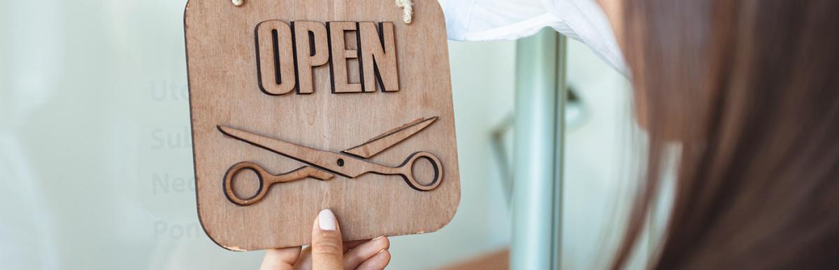 Owner hanging open sign on door for hair salon