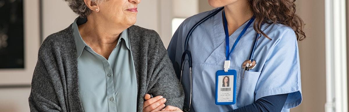 Older woman with cane being helped by nurse in Residential Facility