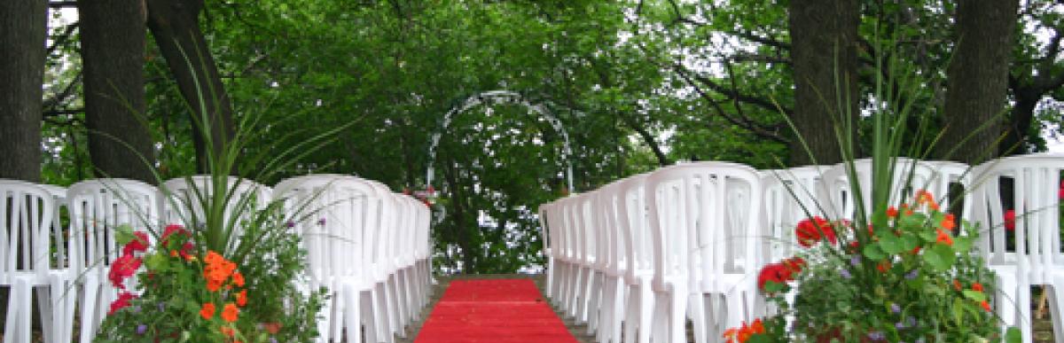 Outdoor weddign with white plastic chairs lined up and a red carpet in the centre aisle