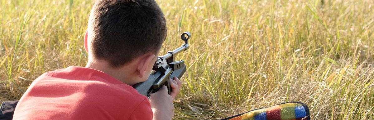 Young boy shooting tin cans with air rifle in a field
