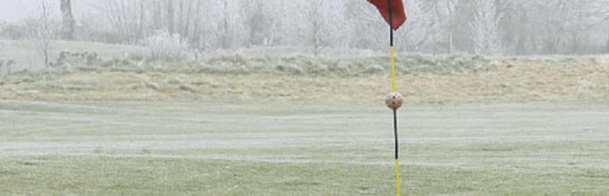 Frost and snow covered golf course with flag on the green.