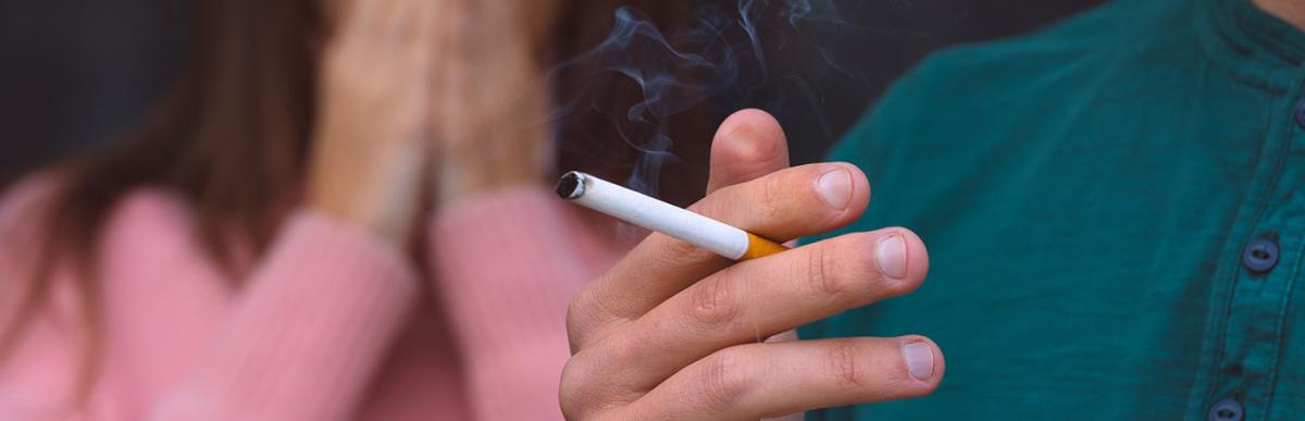 Man smoking cigarette near woman covering her face from cigarette smoke.