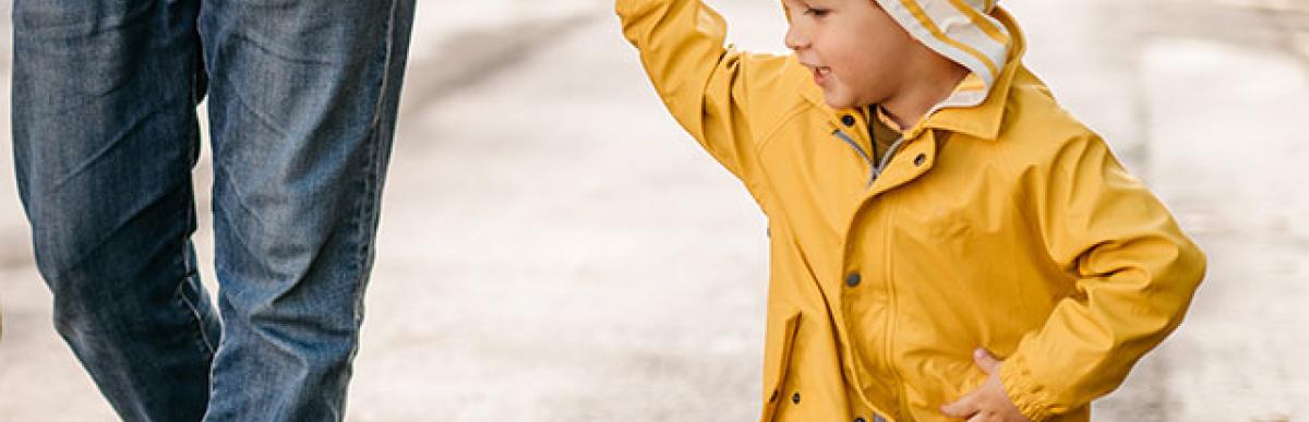 Little boy wearing a yellow raincoat, holding his dad's hand while on a walk outside.