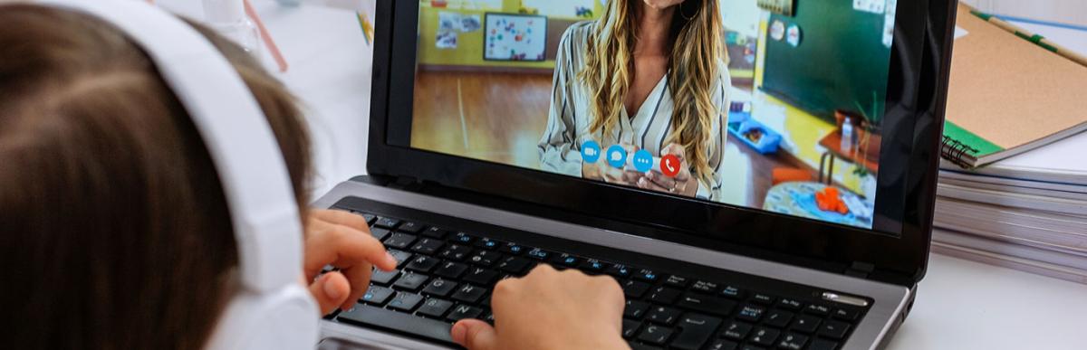 Young girl with headphones using a laptop for school - teacher teaching class via videoconference