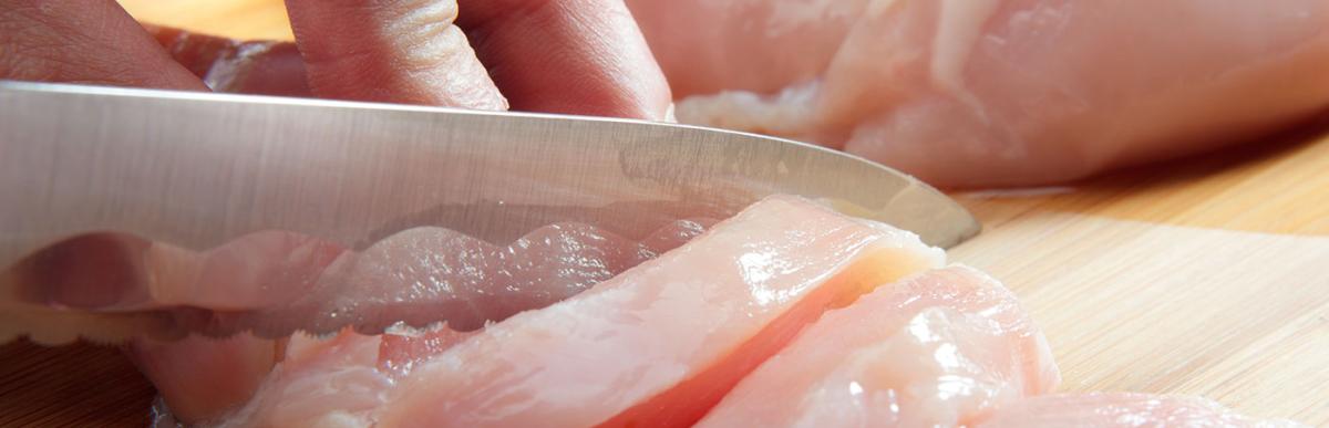 Man's hand cutting raw chicken breast. 