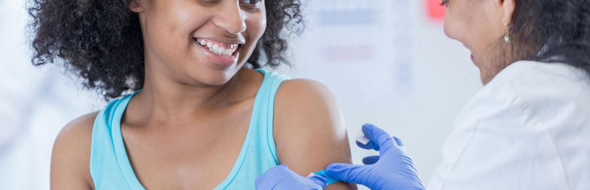 Female doctor puts a bandage on teenage girl's arm after receiving immunization.