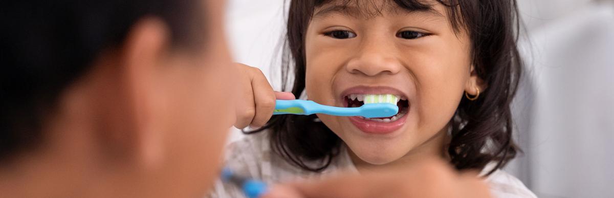 Happy kid and dad having fun while brushing their teeth together in the bathroom sink